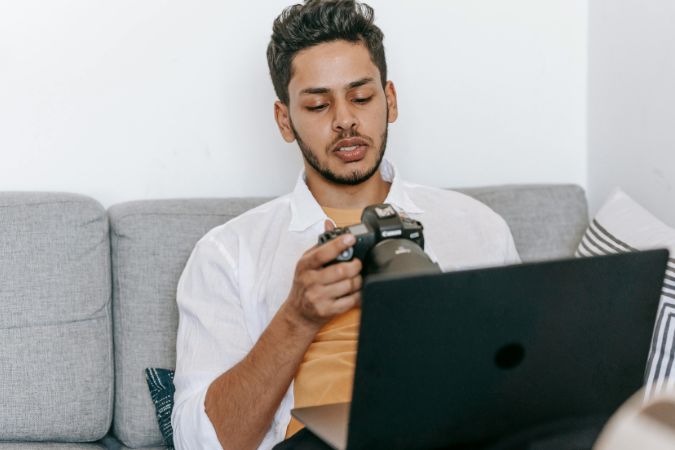 Man with camera sitting on couch using laptop.